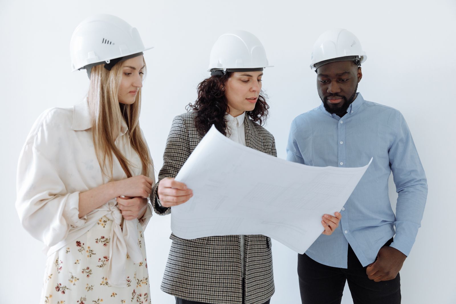 Three people in hard hats looking at a large sheet of paper against a white backdrop
